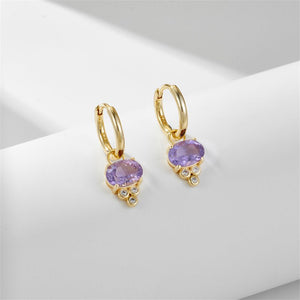 A pair of oval cut amethyst drop hoop earrings, one plated in silver and the other in gold, displayed against a neutral background.