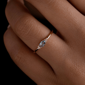 Rose gold ring with a blue gemstone on a person's finger against a dark background