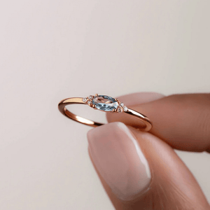Rose gold ring with a blue gemstone held by a hand on a light background