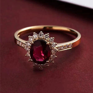 Gold ring with a red gemstone and diamond accents on a dark red background