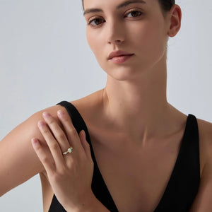 Woman wearing a black top and a ring on her finger against a plain background