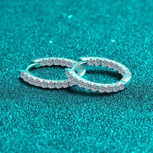 Pair of silver hoop earrings with small diamonds on a teal glitter background
