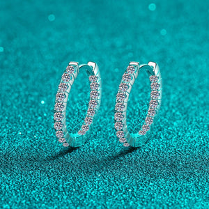 Silver hoop earrings with embedded stones on a teal glittery background