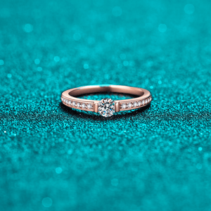 Rose gold ring with a diamond on a teal glittery background