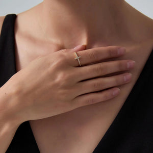 Close-up of a hand wearing a gold ring with a cross design, touching the chest.