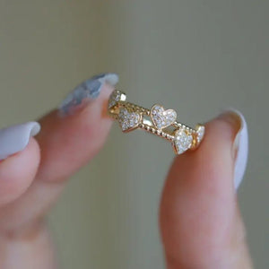 Gold ring with heart-shaped diamonds held between fingers against a neutral background