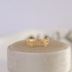 Gold heart-shaped ring on a white cushion with a blurred background