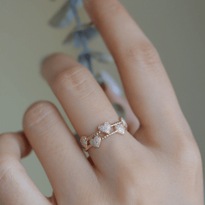 Rose gold ring with floral design on a finger against a blurred background