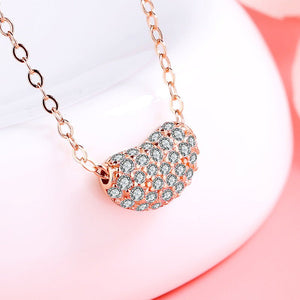 Two bean-shaped sterling silver necklaces with gold plating and cubic zirconia, one displayed in front of the other on a pink background.