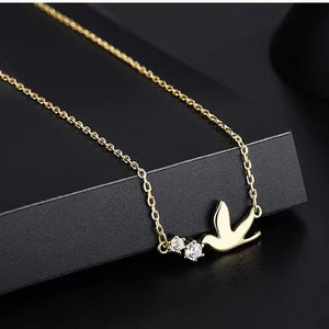 Gold necklace with a bird and heart pendant on a black background