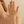 Hand wearing a gold necklace with a green gemstone on a beige background