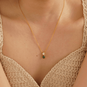 Gold necklace with a green gemstone pendant on a person wearing a beige lace top.