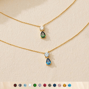 Two gold necklaces with teardrop-shaped gemstones on a beige background