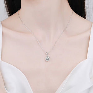 Silver necklace with a heart-shaped pendant worn by a person in a white dress.