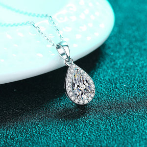 Teardrop-shaped diamond pendant on a chain against a teal background