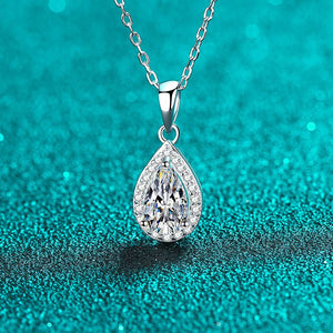 Teardrop-shaped diamond pendant on a chain against a teal glittery background