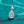 Teardrop-shaped silver pendant with clear gemstone on a turquoise background