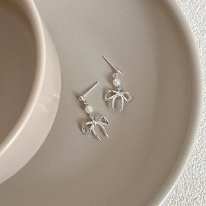 Silver bow-shaped earrings with pearl accents on a beige plate.
