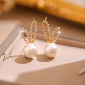 Pearl earrings with gold bunny ear designs on a soft surface