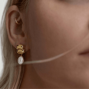 Close-up of a person wearing gold hoop earrings with a pearl accent.