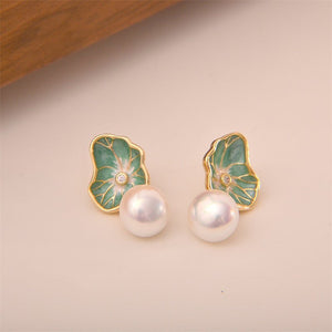 Pearl earrings with green leaf-like designs on a beige background