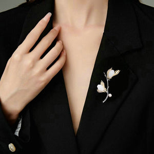 Person wearing a black blazer with a decorative brooch on a neutral background