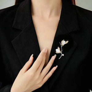Person wearing a black blazer with a decorative brooch on a neutral background