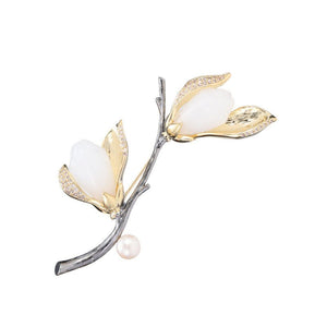 Jewelry piece with gold and silver leaves and a pearl on a white background
