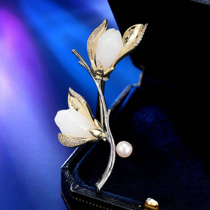 Gold and silver flower brooch with white stones and a pearl on a dark background