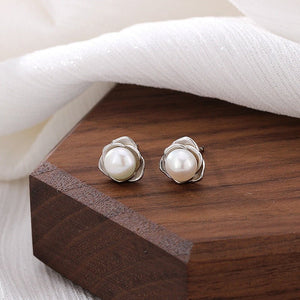 Pearl stud earrings on a wooden surface with a white fabric background