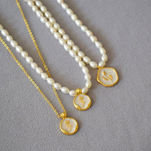 Two pearl necklaces with gold pendants on a gray surface
