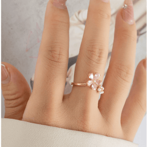 Hand wearing a gold ring with pink gemstones on a neutral background