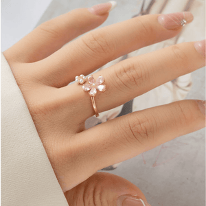 Hand wearing a gold ring with pink gemstones on a neutral background