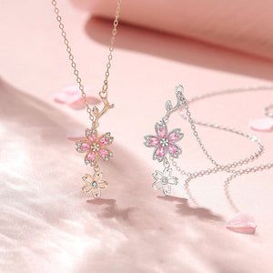Two floral necklaces, one gold and one silver, on a soft pink background.