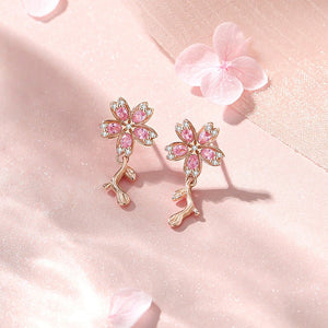 A set of cherry blossom stud earrings in various colors including pink and white, displayed on a soft, floral background.