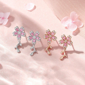 Four pairs of floral earrings with pink gemstones on a soft pink background with flowers.