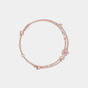 Rose gold bracelet with floral charm on a light gray background