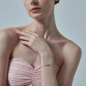 Woman wearing a pink strapless dress with a gold bracelet on a plain background
