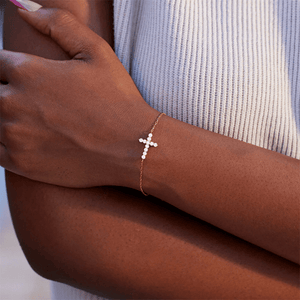 Close-up of a hand wearing a gold bracelet with a cross charm.