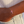 Gold bracelet with a pink and red bead on a wrist, wearing a beige top and denim jeans.