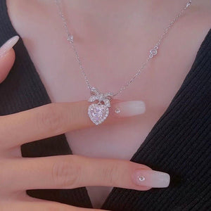 Silver necklace with a heart-shaped pendant held by a hand against a black background