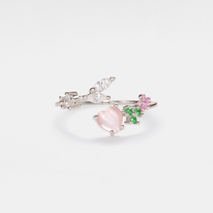 A gold-plated sterling silver stacking bypass ring with a pink heart-shaped gemstone and small leaf details, set against a white background.