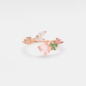 A gold-plated sterling silver stacking bypass ring with a pink heart-shaped gemstone and small leaf details, set against a white background.