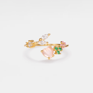 Gold ring with heart-shaped pink gemstone and green and pink gemstones on a white background