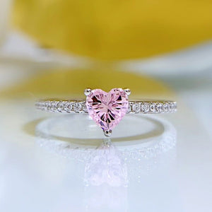 Heart-shaped pink gemstone ring with diamond accents on a white and yellow background