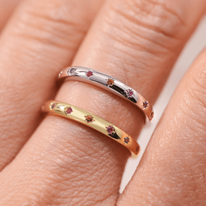 Two gold and silver rings with embedded gemstones on a finger.