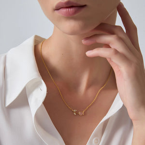 Gold tulip necklace worn by a person with a white shirt on a light background