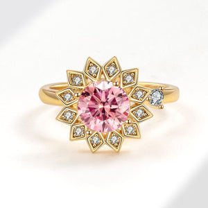 A gold-colored fidget spinner ring with a central pink gemstone and surrounded by clear stones, designed to resemble a sunflower.