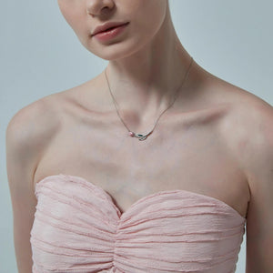 Woman wearing a strapless pink dress and a delicate necklace with a small pendant on a plain background