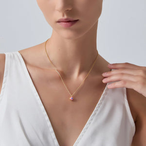 Woman wearing a gold necklace with a colorful pendant on a plain background